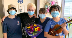 A family of three volunteers smiling with their senior client, who is holding a bouquet of flowers.