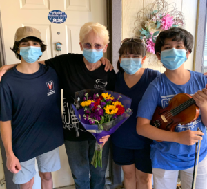 A family of three volunteers smiling with their senior client, who is holding a bouquet of flowers.