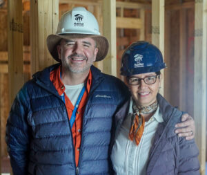 Jorge and Ana in Habitat for Humanity hard hats, smiling and embracing in their soon-to-be home.